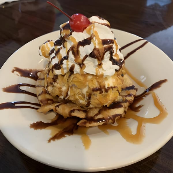 Fried ice cream with whipped cream, chocolate, caramel, and a cherry on a white plate.
