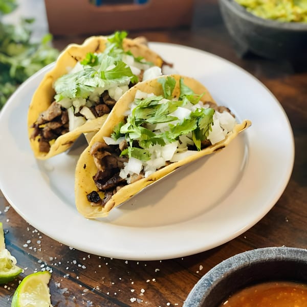 Two Fiesta Grande Mexican Grill tacos with meat, onions, and cilantro on a white plate.
