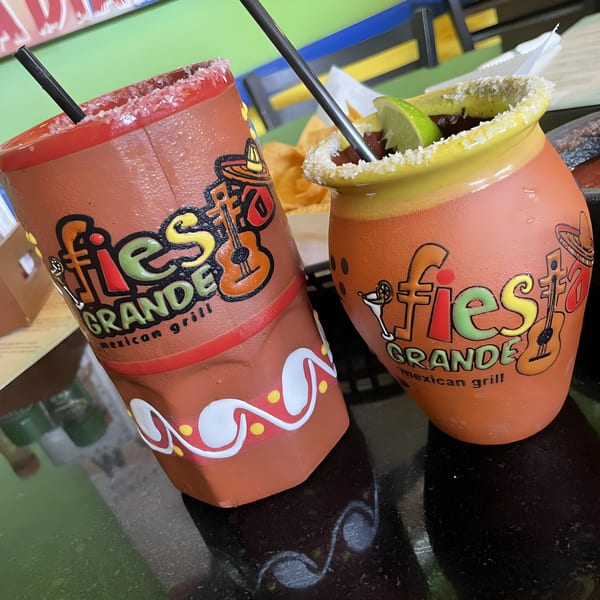 Two Fiesta Grande Mexican Grill branded drinks, one with a lime, on a dark table.