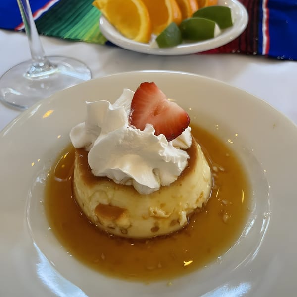 Flan dessert with whipped cream and a strawberry slice, surrounded by caramel sauce on a white plate.