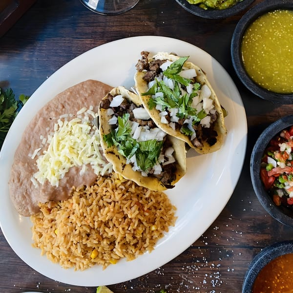 Two carne asada tacos with cilantro and onions, served with refried beans and rice.